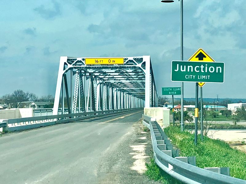 Junction city limit sign in front of a steel bridge into Junction TX